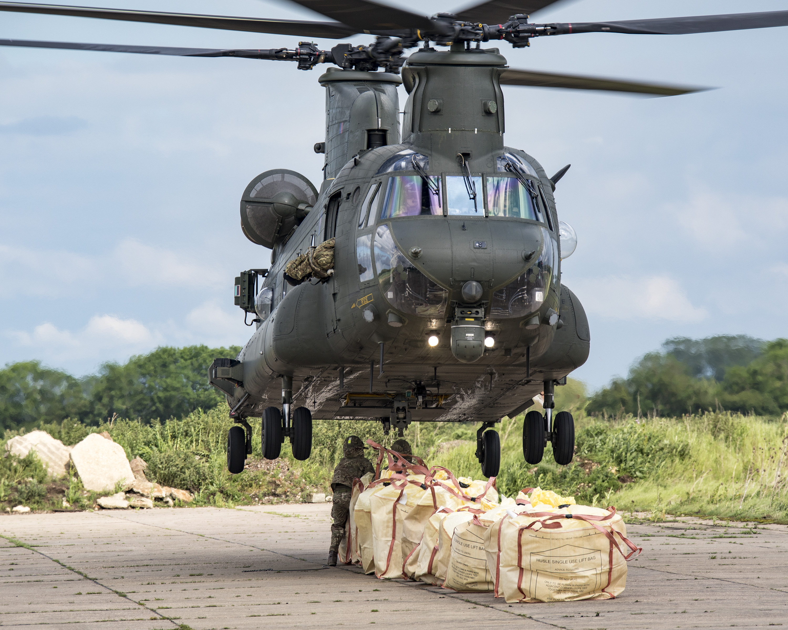 Image shows aviators tending to cargo load underneath hovering helicopter.